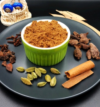 Biryani Masala Powder is in green bowl on black plate with some gram masala