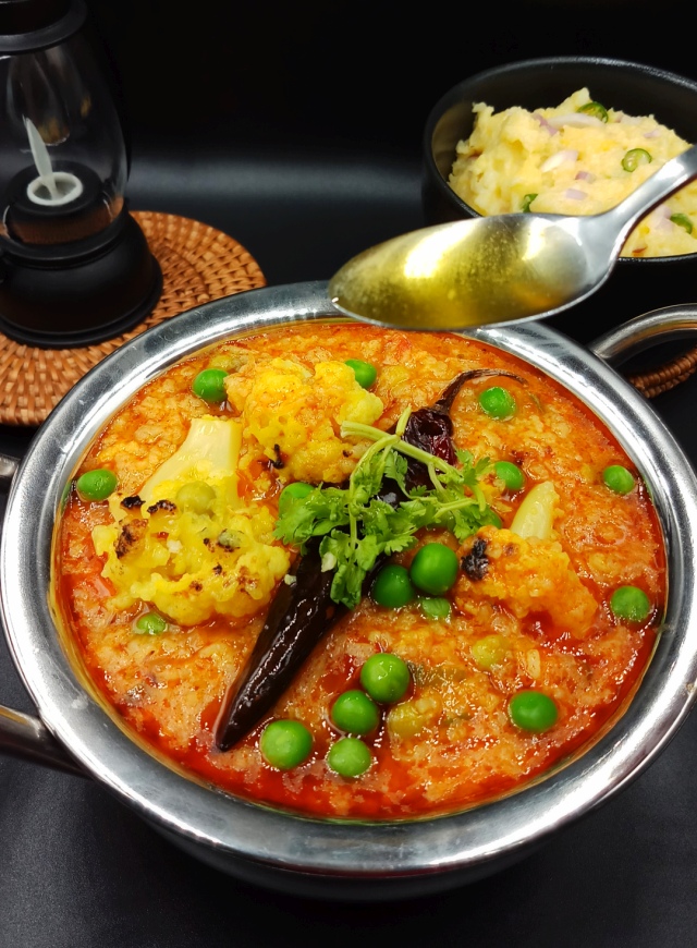 A bowl of steaming masala khichdi garnished with fresh coriander leaves and whole red chili.