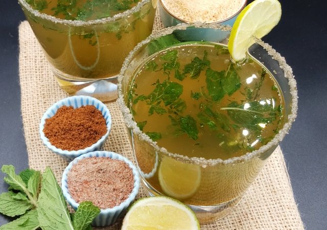 Masala Shikanji Recipe (Indian lemonade) in a whisky glass on jute mat with mint leave, lemon, sugar, salt and roasted cumin powder.