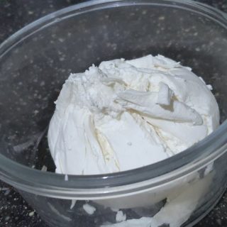 Creamy hung curd in a transparent bowl on black surface.