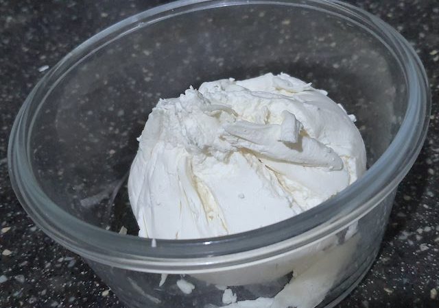 Creamy hung curd in a transparent bowl on black surface.