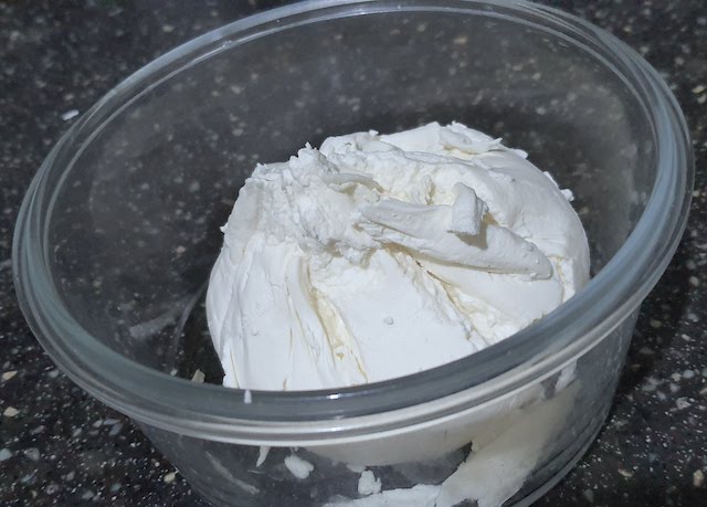 Creamy hung curd in a transparent bowl on black surface.