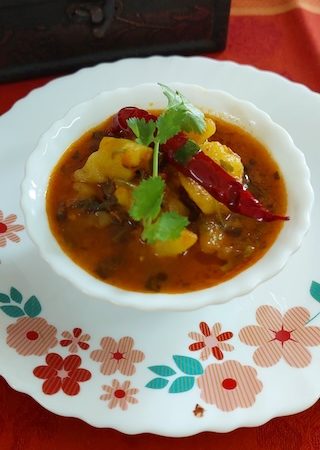 A bowl filled with savory spicy potato curry garnished with fresh cilantro leaves.