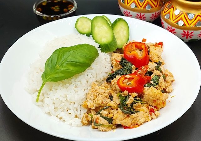A sizzling plate of Thai Basil Chicken with vibrant colours of red chilies and green basil leaves, served over steaming rice.