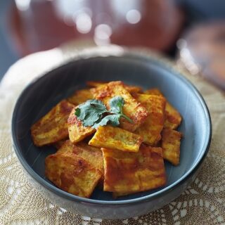 Crispy raw banana fritters (kachche kele ke pakode) served on a plate with green chutney and hot masala chai.