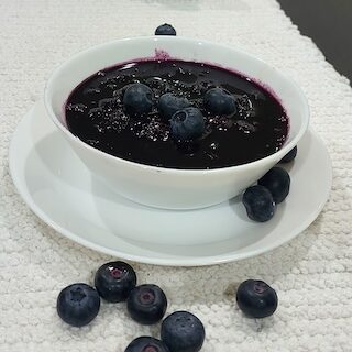 Homemade blueberry sauce in a bowl with fresh blueberries on the side