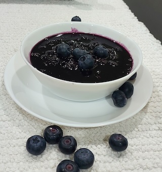 Homemade blueberry sauce in a white bowl with fresh blueberries.
